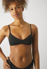 Svart bikinitop med tunna band, med en triangelform och slätt tyg. Designen har en minimalistisk stil och subtila sömnadsdetaljer.