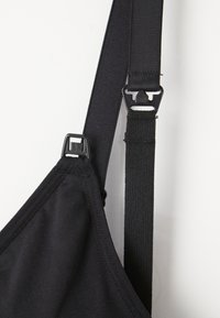 Tuvas plāns melns auduma siksna ar plastmasas skavām un elastīgu joslu uz melna apģērba pret baltu fona.