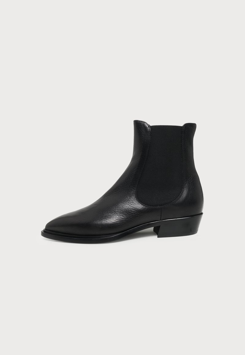 Bottine Chelsea en cuir noir avec panneau latéral élastique et petit talon empilé sur fond clair uni.