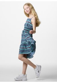 Blauwe jurk met een patroon en dunne bandjes, met geometrische ontwerpen in groen en burgundy. Gestyld met witte sneakers.