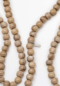 Collana di perline realizzata in materiale testurizzato di colore marrone chiaro con motivi maculati variabili. Include un piccolo tag in argento attaccato.