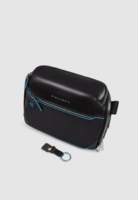 Zwarte lederen tas met een glanzende afwerking, contrasterende blauwe stiksels, een bovenste ritssluiting en een afneembare sleutelhangerbevestiging. Rechthoekige vorm.