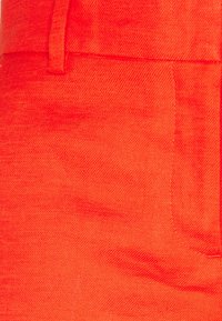 Červená látka s texturovaným povrchem, obsahující siluetu boční kapsy a viditelné švy. Materiál se zdá být lehký a prodyšný.