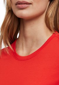 Rode katoenen T-shirt met een ronde hals. Gladde textuur en korte mouwen, met minimale stikseldetails rond de halslijn.