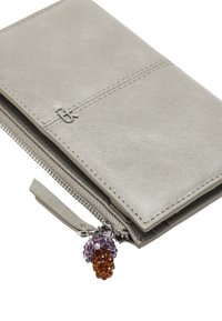 Szary portfel ze skóry o gładkiej fakturze, zamykany na zamek błyskawiczny, z zawieszką ozdobioną fioletowymi i pomarańczowymi koralikami. Posiada subtelne wytłoczone logo.