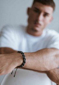 Black bead bracelet with round beads and adjustable cord, worn on a wrist, showcasing a smooth texture against a light backdrop.