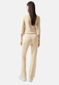 Beige gestricktes Oberteil und passende Hose mit 3/4-Ärmeln, schlankem Schnitt und zwei Gesäßtaschen an der Hose. Glatte Textur.