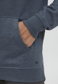 Navyblauwe hoodie van zachte stof, met een kangoeroezak, ribgebreide manchetten en een klein logo-accent aan de onderkant.