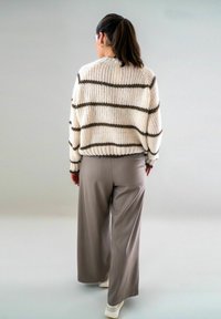 Roomkleurige en bruine gestreepte gebreide trui met een losse pasvorm, gecombineerd met lichtgrijze wijde broeken en witte sneakers.
