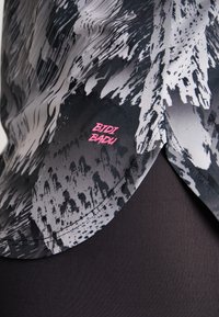 Top a maniche corte con un motivo astratto in nero e grigio, realizzato in tessuto morbido, con un logo "BIDI BADU" rosa sull'orlo.