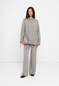 Sweatshirt de algodão cinza com cordão, combinado com calças largas a condizer. O modelo segura uma pequena bolsa rosa com cordão. Design até ao chão.