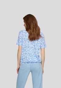 Kurzärmliges T-Shirt in Hellblau mit floralem Muster, das einen lockeren Schnitt und weichen Baumwollstoff aufweist. Die Rückansicht zeigt dieKontinuität des Designs.