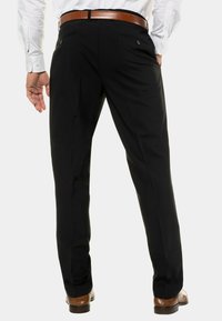 Pantalones de traje negros con una textura suave, que presentan bolsillos traseros y un ajuste ceñido. Un cinturón y zapatos de cuero marrón completan el look.