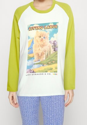 Personne portant un t-shirt à manches longues blanc et vert avec un grand chaton, un paysage et le texte "Living Large" à l'avant.