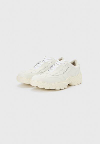 Λευκά chunky sneakers με υφή στη σόλα, σχέδιο με κορδόνια και λογότυπο "ROMBAUT CORE" στο πλάι, τοποθετημένα σε απλό φωτεινό υπόβαθρο.