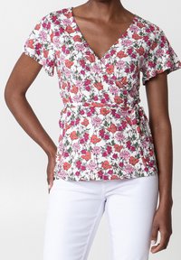 Blommig omlottopp med korta fladdriga ärmar, med rosa och orange blommor på vit bakgrund, knuten i midjan med en texturerad finish.