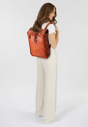 Sac à dos en cuir marron avec fermeture à rabat et détail de boucle. Présente une forme rectangulaire et une finition texturée, porté sur le dos.