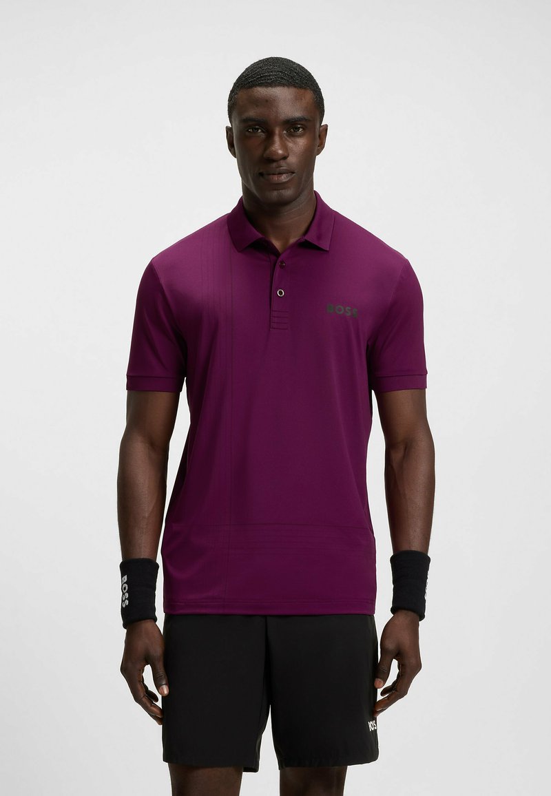 Dunkelviolettes Polo-Shirt mit kurzen Ärmeln, knöpfbarem Kragen und kontrastierendem grünen Logo. Besitzt eine glatte Textur und ein elegantes, körperbetontes Design.