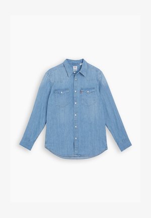 Light blue denim shirt with long sleeves, pointed collar, and two chest pockets. Features button closure and curved hem.