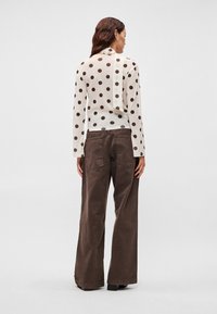 Biała bluzka z długim rękawem w brązowe kropki, z ozdobą na plecach, zestawiona z brązowymi spodniami o szerokich nogawkach. Bawełniana, teksturowana tkanina.