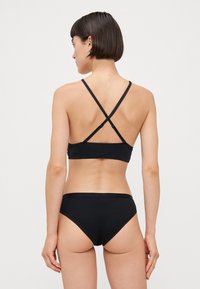 Black bikini featuring a bralette top with crisscross straps at the back and matching bottom with a seamless waistband. Smooth texture.