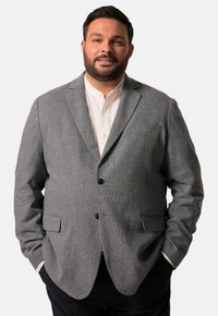 Szary blezer w wzór houndstooth z wykładanymi klapami, dwoma przednimi kieszeniami i czarnymi guzikami, noszony na białej koszuli. Pokazany dopasowany krój.