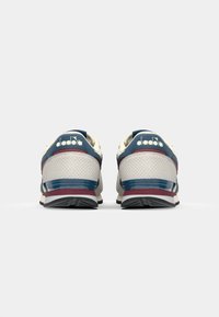 White and navy blue athletic shoes with perforated detailing, contrasting maroon accents, and textured rubber soles. Diadora branding on back.