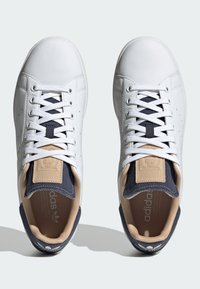 Valged nahast sneakerid tumesiniste aktsentidega, tekstuuriga keel, klassikaline paeltesüsteem ning logo detailid kandadel ja keeles.