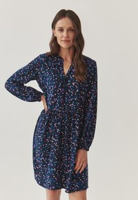 Marine jurk met lange mouwen, een kraag, een gather taille en een patroon van roze en blauwe bladvormen op een donkere achtergrond.