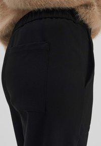 Pantalons noirs en tissu doux, avec une coupe décontractée, une taille élastique et une poche arrière unique. Couture standard et aucun motif visible.