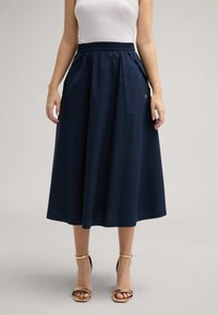 Marineblaue Midirock mit strukturierter Oberfläche, elastischem Bündchen, seitlichen Taschen und einem kleinen Logodetail an der Taille.