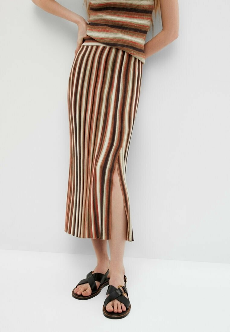 Femme portant une jupe midi rayée marron, crème et rouille avec une fente latérale, associée à un haut sans manches assorti et des sandales noires à brides croisées.