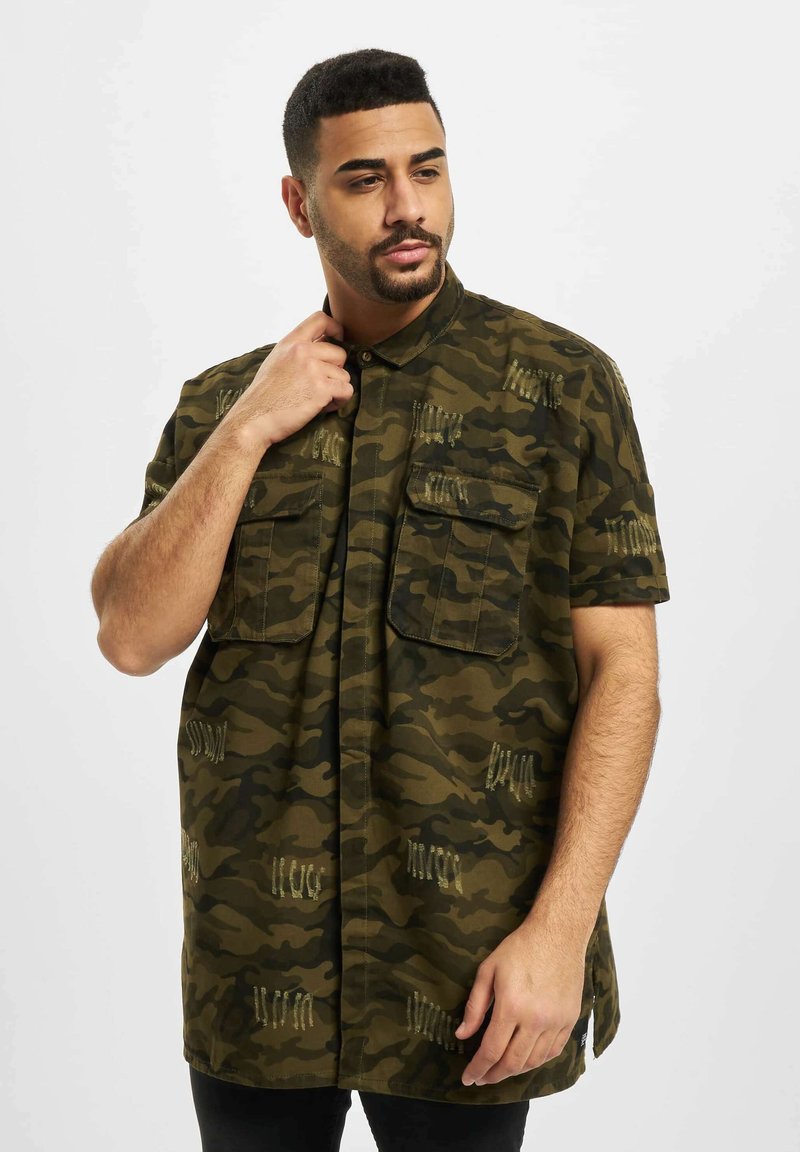 Camicia a maniche corte con motivo camouflage, realizzata in tessuto leggero, dotata di due tasche sul petto e cuciture decorative in verde e beige.
