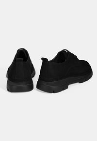 Chaussures à lacets en suédine noire avec une tige texturée, un bout arrondi et une semelle en caoutchouc épaisse. Onglet à l'arrière pour un enfilage facile.