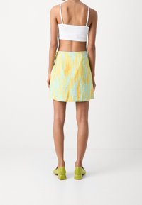 Una mini falda de rayas en azul pastel y amarillo, hecha de un tejido texturizado, combinada con zapatos de tacón bloque verde y una camiseta corta blanca.