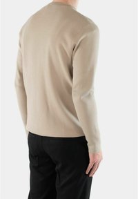 Beżowy sweter z dzianiny z długimi rękawami i okrągłym dekoltem, charakteryzujący się gładką, miękką teksturą. Noszony z czarnymi spodniami.