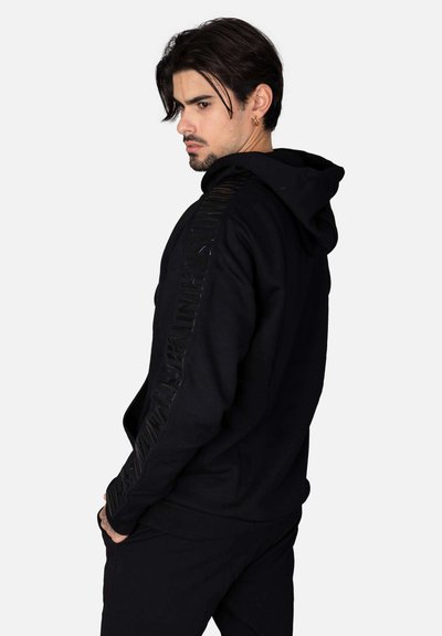 Felpa nera con cappuccio realizzata in tessuto morbido, con un pannello laterale testurizzato e con logo. Dotata di tasca a marsupio, cappuccio regolabile tramite cordino e polsini a coste.