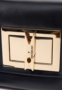 Svart teksturert lærveske med en gullfarget lås med "LOVE MOSCHINO" gravering. Låsen har et unikt design som likner en klesklype.