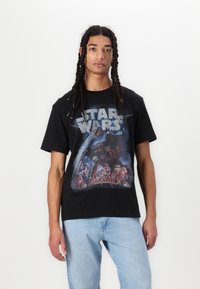Černé bavlněné tričko s barevným potiskem "Star Wars" na přední straně, s krátkým rukávem a volným střihem, spárované s světlomodrými džíny.