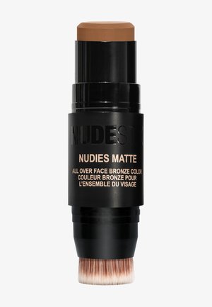 Black cylindrical makeup stick with a brown cream top. Features a built-in brush at the bottom for application. Labels are in gold.