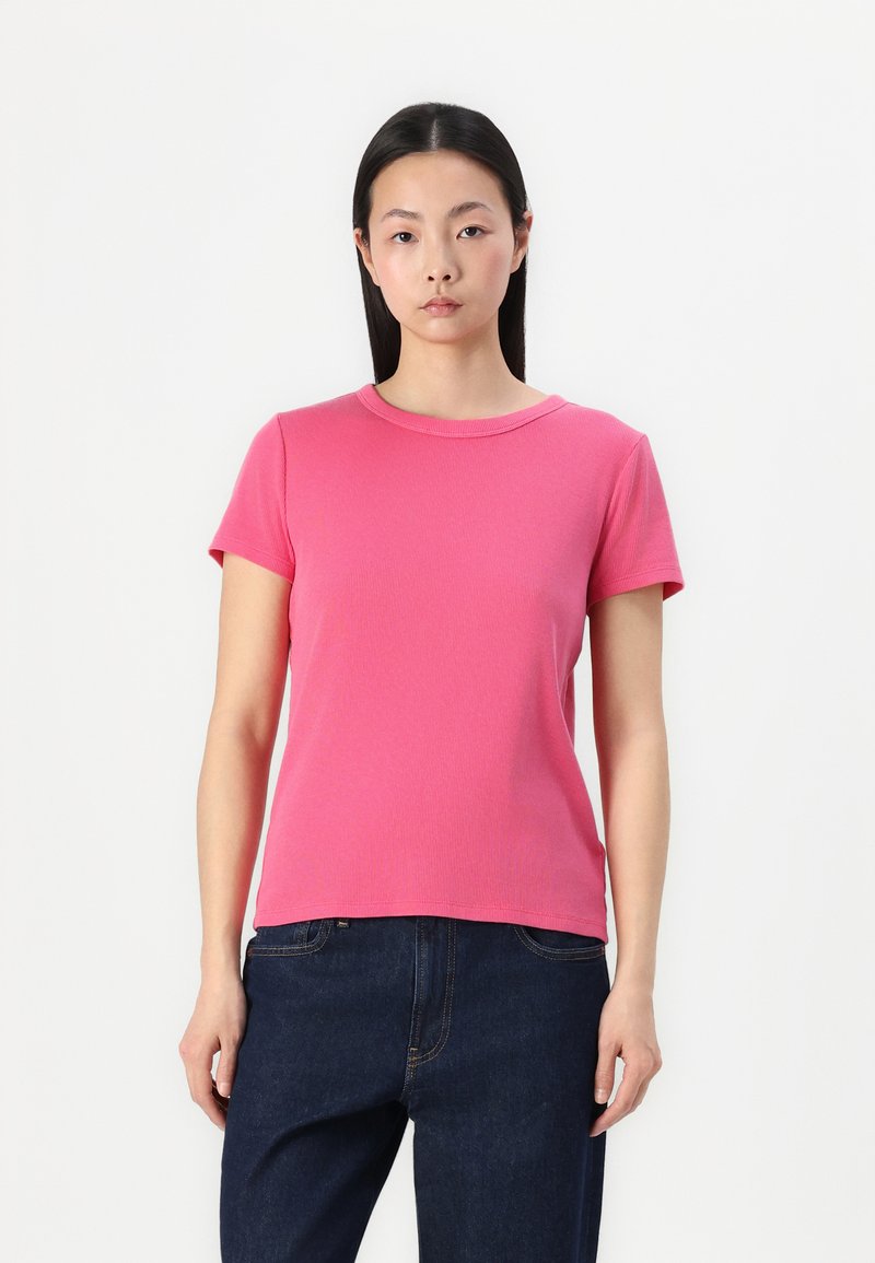 T-shirt rose à manches courtes avec col rond et silhouette ajustée, fabriqué en tissu doux et associé à un jean bleu foncé.
