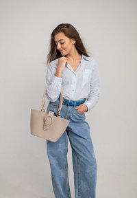 Borsa tote beige con dettaglio a fibbia rotonda, abbinata a una camicia azzurro chiaro con bottoni e jeans a gamba larga con motivo a stelle.