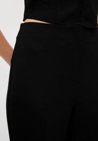 Pantalones negros ajustados con una suave textura y una cinturilla de tiro medio, que cuentan con bolsillos laterales y un diseño sin costuras a lo largo de la cadera.