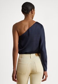 Ναυτικό μπλε σατέν τοπ με σχεδίαση ενός ώμου· το άλλο μανίκι είναι μακρύ. Συνδυάζεται με ανοιχτόχρωμο εφαρμοστό παντελόνι με πίσω τσέπες.