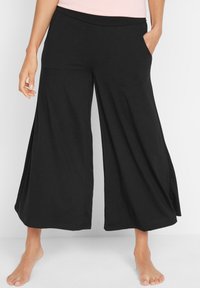 Pantaloni neri a gamba larga realizzati in tessuto morbido, dotati di una vita elasticizzata e due tasche laterali, che arrivano appena sopra le caviglie.