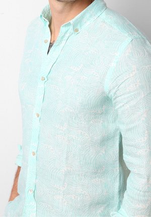 Vaaleansininen pellavapaitapusero, jossa on aaltoileva kuvio, kaulus ja käännetyt hihat, joissa on beigejä nappeja.