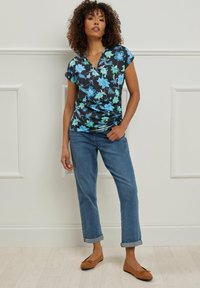 Top de manga corta con escote en V en color navy con un patrón floral en azul y verde, combinado con jeans de puño enrollado y bailarinas marrones.