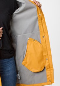 Yellow waterproof jacket with a grey fleece lining; features snap closures, a side pocket, and contrasting material textures.