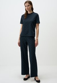 Set di top e pantaloni con motivo nero e teele, caratterizzato da un design geometrico a diamante. Tessuto morbido, vestibilità rilassata, maniche corte e gambe larghe.