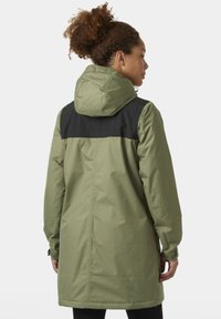 Parka impermeable de color verde oliva con una parte superior negra. Cuenta con capucha, mangas largas y un corte que llega a la mitad del muslo. Textura suave.
